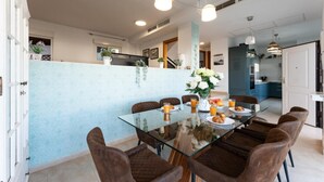 Un espace repas moderne avec une table en verre, des chaises recouvertes d’un tissu marron et un mur d’accent bleu clair.
