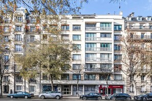 A multi-story building with balconies, a storefront, and parked cars. - Elegant Apartment Paris 16th - Near the Seine (Paris)