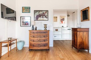 Ein Zimmer mit Holzböden, einem Holzschrank, einem an der Wand befestigten Fernseher und verschiedenen gerahmten Kunstwerken.