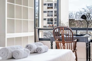 Ein Hotelzimmer mit einem Bett, einem Holzstuhl, einem Schreibtisch und Blick auf ein Gebäude durch ein Fenster.
