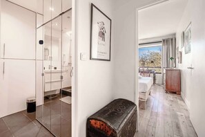 A modern interior with a glass door leading to a bathroom, a framed artwork on the wall, and a bench in the foreground. - Elegant Apartment Paris 16th - Near the Seine (Paris)
