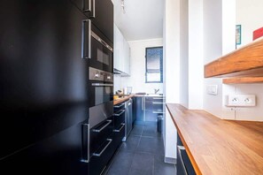A modern kitchen with black cabinets, stainless steel appliances, and a wooden countertop. - Elegant Apartment Paris 16th - Near the Seine (Paris)