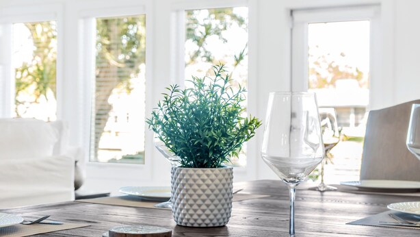 A dining table with a potted plant, a wine glass, and plates. - Waterfront, Fishing, Firepit @ The Pier Cottage (New Port Richey)