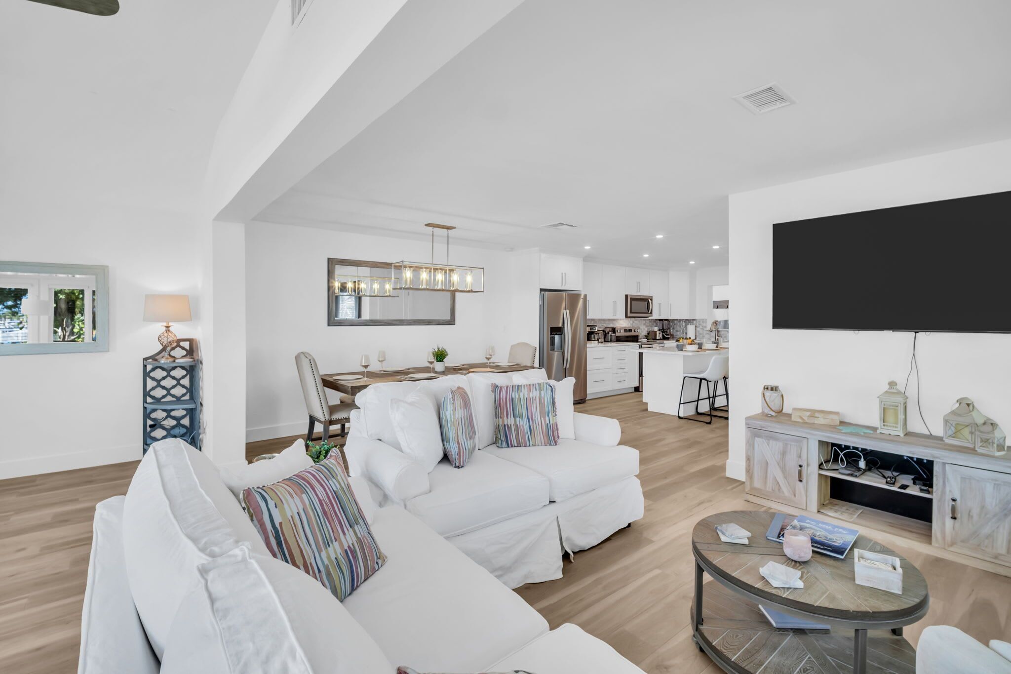 Ein modernes Wohnzimmer mit einer Couch, einem Essbereich, einer Küche und einem an der Wand befestigten Fernseher.