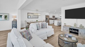 A modern living room with a sofa, a dining area, a kitchen, and a TV mounted on the wall. - Waterfront, Fishing, Firepit @ The Pier Cottage (New Port Richey)
