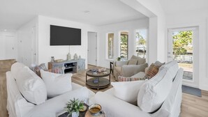A spacious living room with a large flat-screen TV, two sofas, a coffee table, and a bookshelf. - Waterfront, Fishing, Firepit @ The Pier Cottage (New Port Richey)