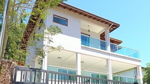 Ein modernes, zweistöckiges Haus mit Balkon, geschlossenem Eingangsbereich und blauem Himmel.