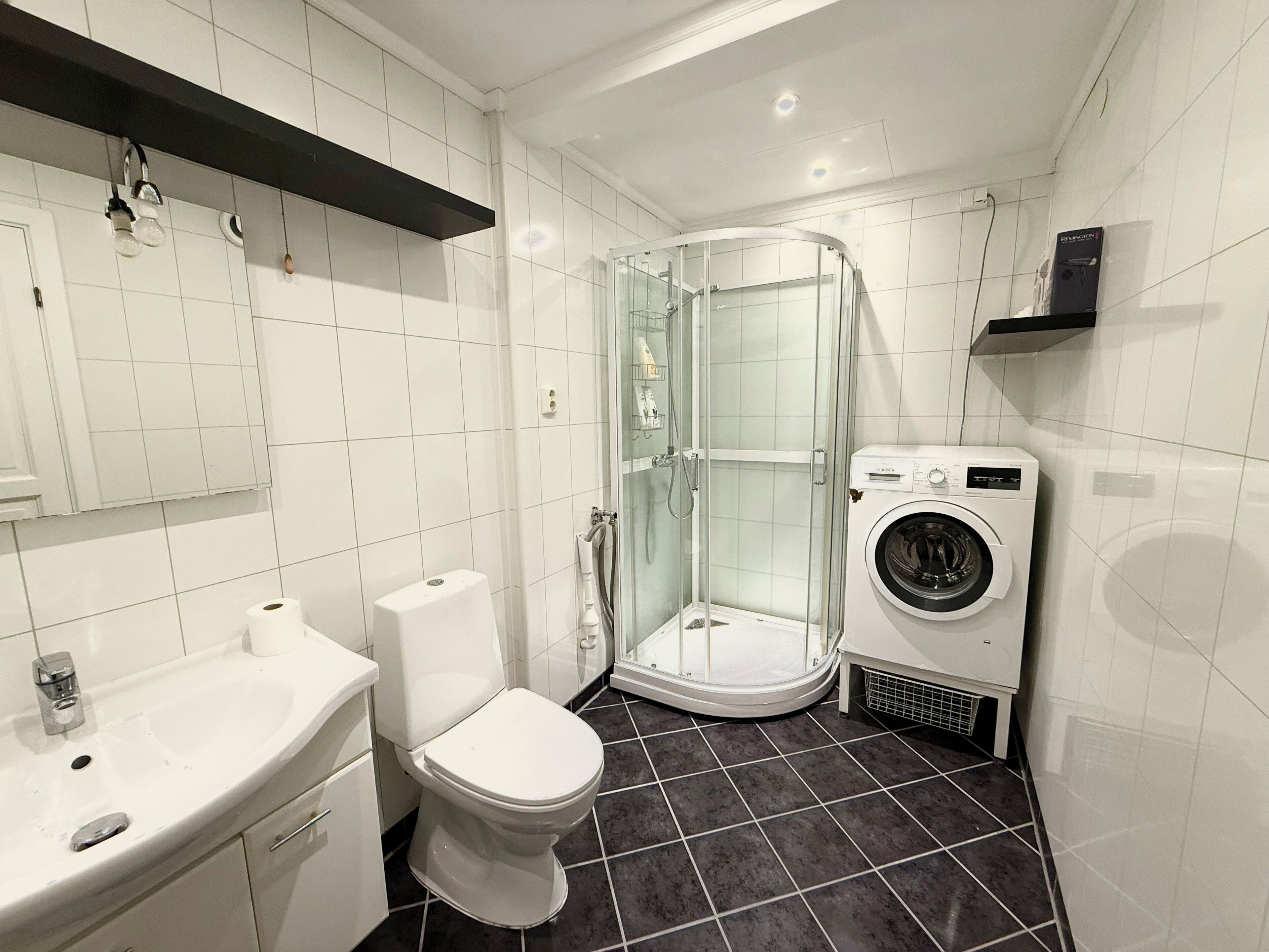 A modern bathroom with a toilet, sink, glass shower enclosure, and a washing machine.