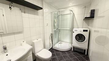 A modern bathroom with a toilet, sink, glass shower enclosure, and a washing machine.