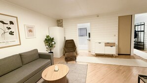 A modern living room with a grey sofa, a round wooden coffee table, a potted plant, and a white cabinet.
