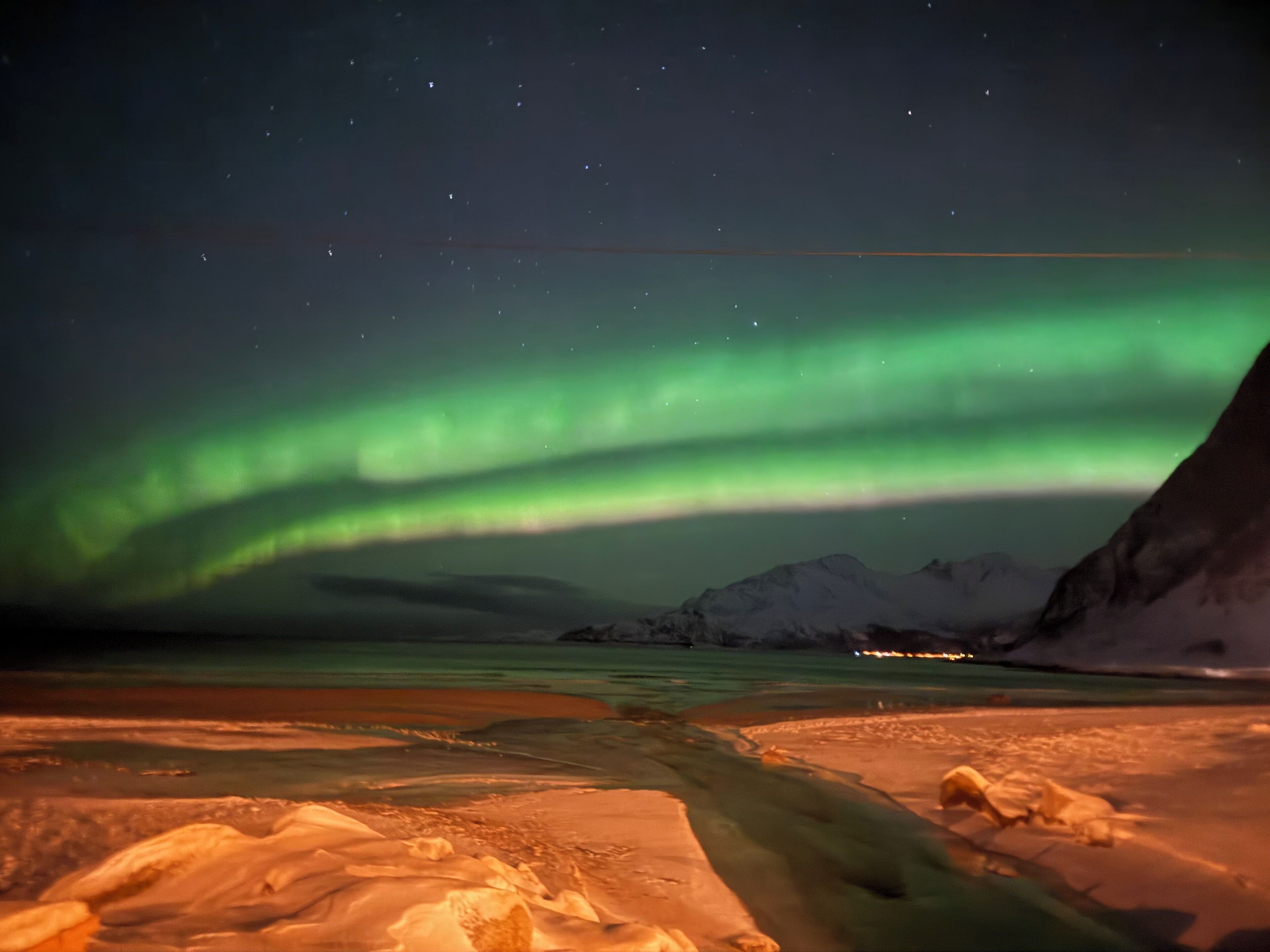 A snowy landscape with a river flowing through it, under a night sky with the aurora borealis.