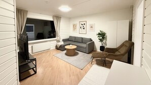 A modern living room with a grey sofa, a round coffee table, a brown armchair, and a TV on a stand.