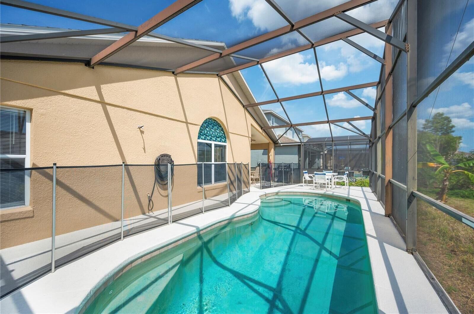 Une piscine extérieure couverte, dotée d’une structure en verre, un espace patio avec des chaises et une vue sur le paysage environnant.