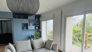 A modern living room with a grey sofa, a large window, and a blue wall with shelves. - Family home 2 steps from the port and downtown. Sleeps 8. (Vannes)