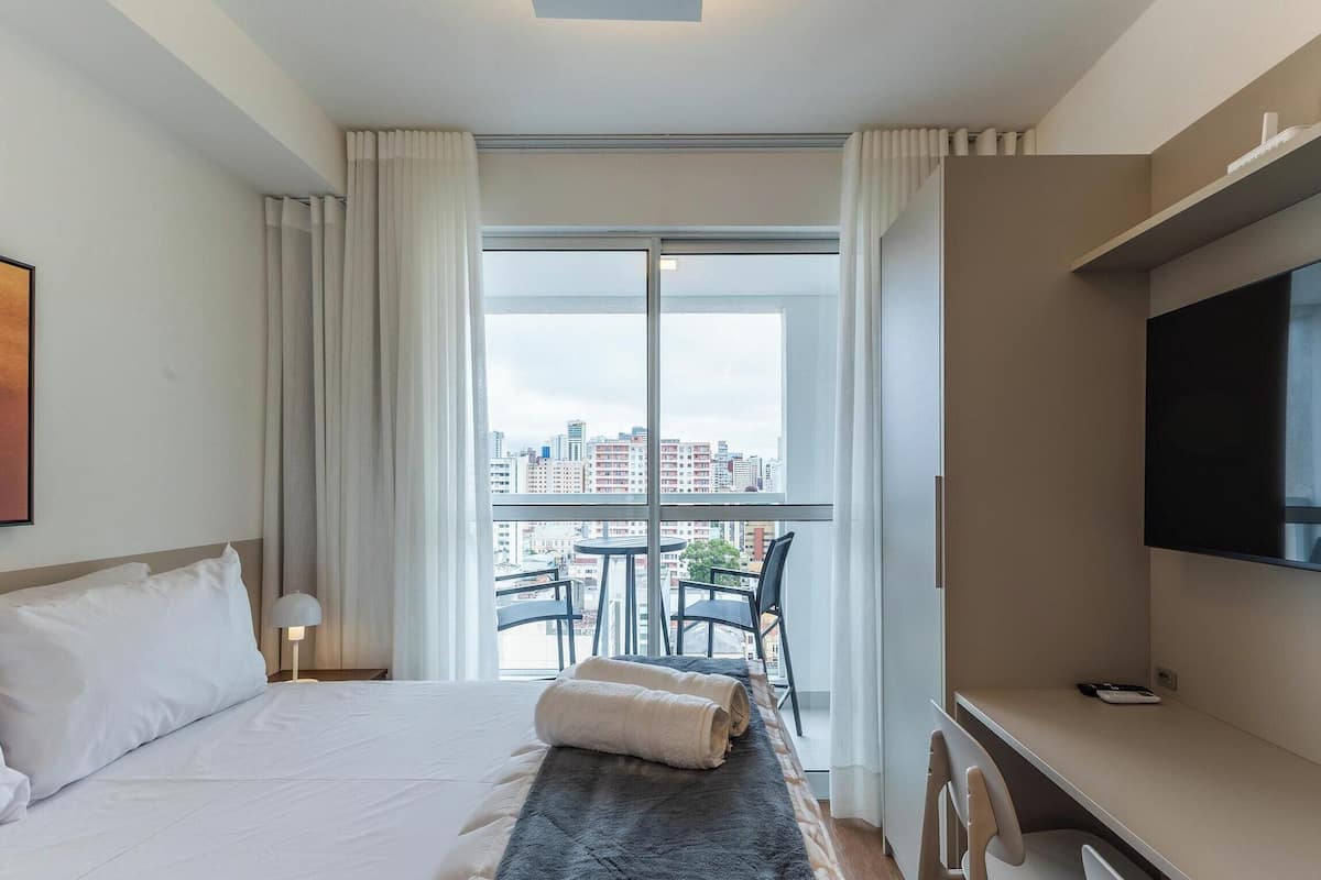 Habitació d'hotel amb un llit, una taula de treball, televisió i un balcó amb vista a la ciutat.