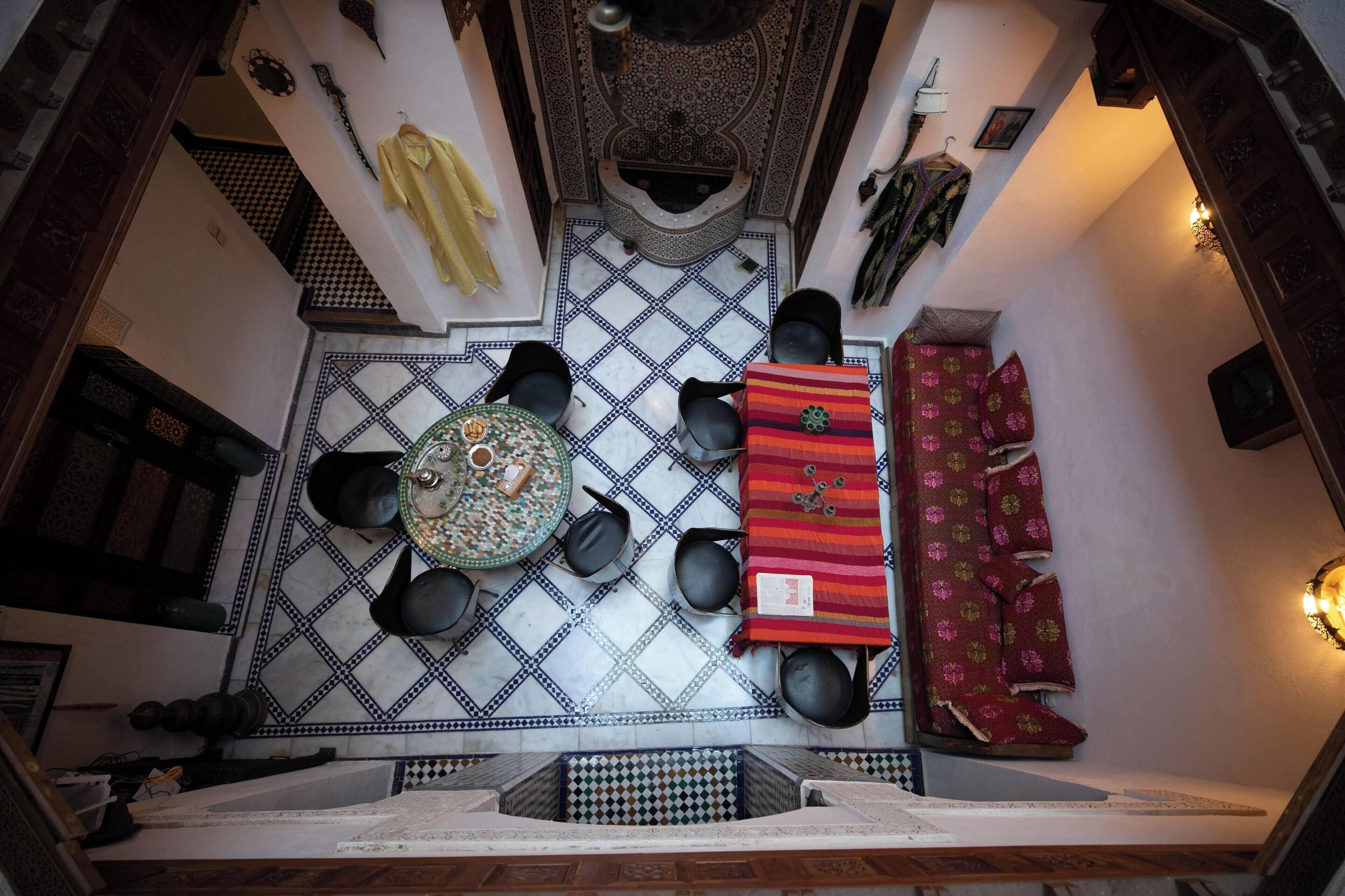 Una habitación con piso a cuadros, una mesa redonda con sillas, una alfombra estampada y una cortina roja.