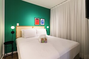 Ein ordentlich bezogenes Bett mit weißen Leinen, ein hölzernes Kopfteil und zwei gerahmte Kunstwerke an der Wand.