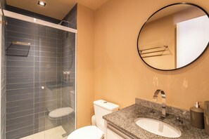 Ein Badezimmer mit Duschkabine, weißer Toilette, Waschtisch mit Granitplatte und rundem Spiegel.