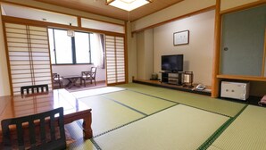 Perinteinen japanilainen huone, jossa on tatamimatto, puinen pöytä, tuolit, televisio ja kaappi.