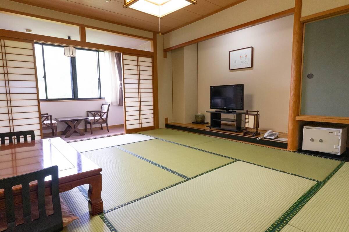 Une pièce de style japonais traditionnel, avec un sol recouvert de tatamis, une table en bois, des chaises, un téléviseur et un meuble.
