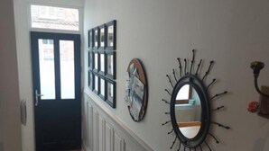 Un couloir doté d’un plancher en bois, d’une porte noire et d’œuvres d’art décoratives murales, notamment un miroir et des tableaux encadrés.
