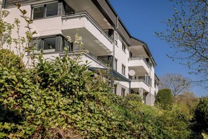 Un immeuble à plusieurs étages doté de balcons, entouré d’une végétation luxuriante.