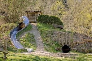 A playground with a slide, a wooden bench, and a log cabin in a wooded area. - 5 minutes from the Green Hill Bikepark and the Hunau slope Family apartment! (Schmallenberg)