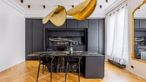 A modern dining area with a marble table, black chairs, and a large gold chandelier. - Avenue Niel - Place des Ternes - 2 chambres - Luxe (Paris)