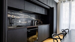 A modern kitchen with dark cabinetry, a marble backsplash, and a wooden herringbone floor. - Avenue Niel - Place des Ternes - 2 chambres - Luxe (Paris)