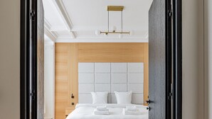 A modern bedroom with a large bed, a wooden headboard, and a herringbone-patterned floor. - Avenue Niel - Place des Ternes - 2 chambres - Luxe (Paris)
