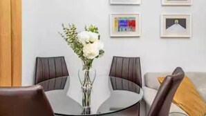 A dining area with a round glass table, two chairs, and a vase with flowers. There are framed pictures on the wall. - Balmoral Residence - 30 min to Glasgow & Edinburgh (Falkirk)