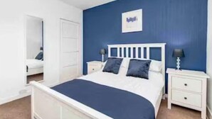 A bedroom with a bed, white nightstands, and a blue accent wall. - Balmoral Residence - 30 min to Glasgow & Edinburgh (Falkirk)