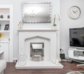 Un salon moderne avec une cheminée blanche, un téléviseur fixé au mur et un lustre.