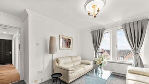 A modern living room with a beige sofa, a glass coffee table, a floor lamp, and a view of the outside through large windows. - Ochil View 30 mins to Edinburgh (Falkirk)