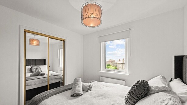 A modern bedroom with a large bed, a mirror with a gold frame, a window with a view, and a unique ceiling light fixture. - Ochil View 30 mins to Edinburgh (Falkirk)