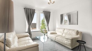 A modern living room with a beige leather sofa, a glass coffee table, and a black side table. - Ochil View 30 mins to Edinburgh (Falkirk)