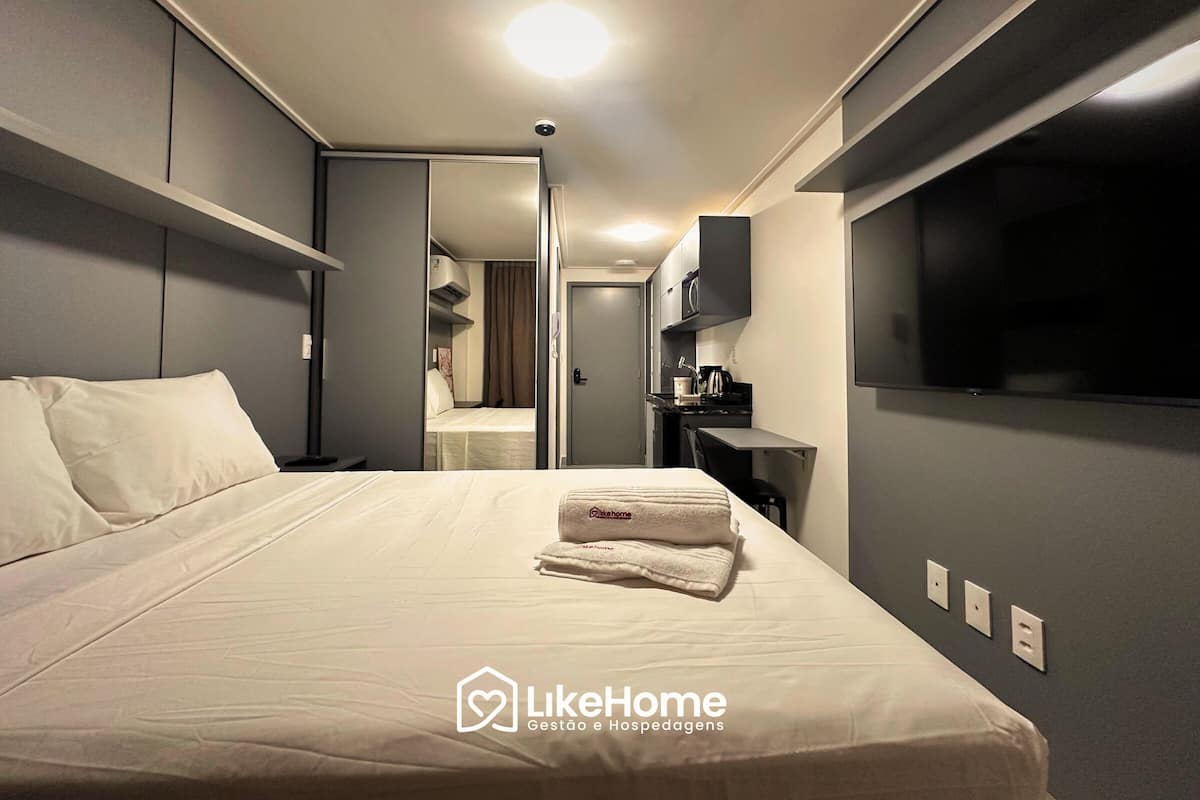 Une chambre d’hôtel avec un grand lit, un téléviseur à écran plat, une petite kitchenette et une salle de bain visible à travers une porte ouverte.