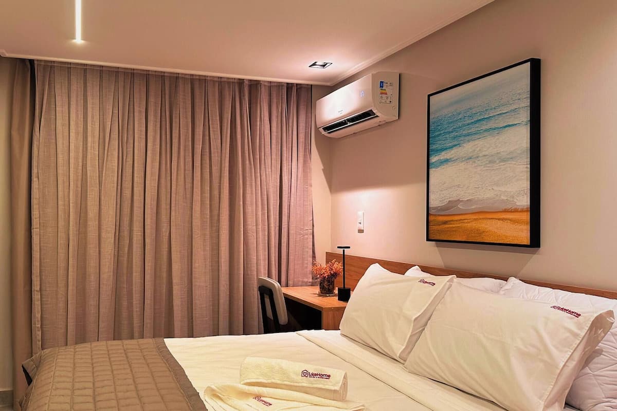 Une chambre d’hôtel avec un lit, un bureau, un climatiseur, un tableau et un rideau.