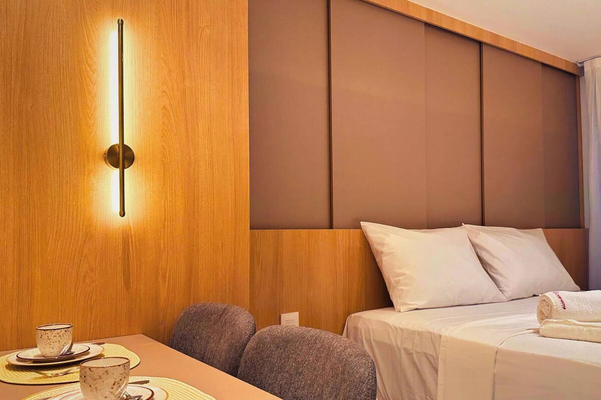 Une chambre d’hôtel avec une armoire en bois, un lit avec du linge de maison blanc et une table sur laquelle se trouvent une tasse et une soucoupe.