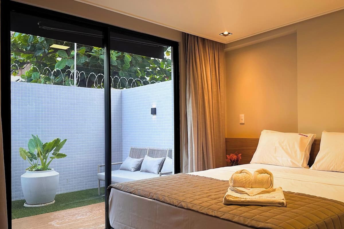 Une chambre d’hôtel avec un lit, un petit coin salon agrémenté d’une plante, et une vue sur la verdure environnante.