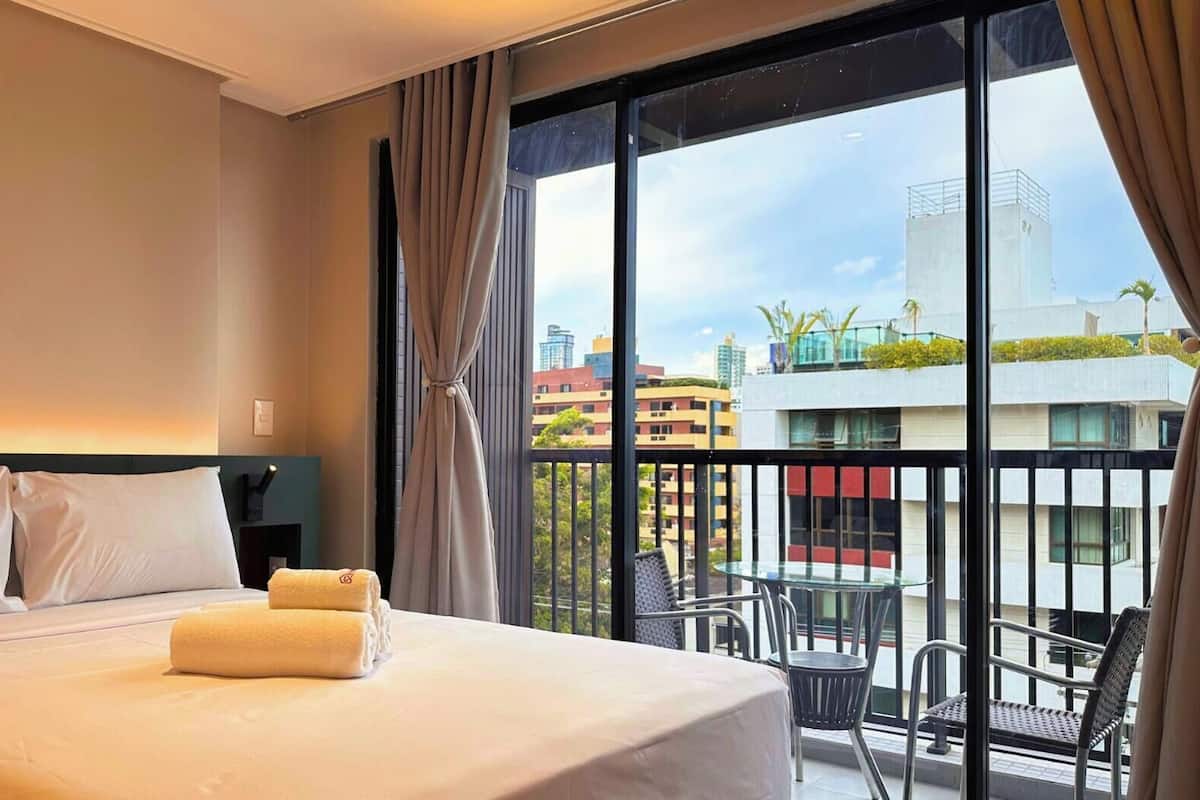 Une chambre d’hôtel avec un grand lit, un balcon avec une table et des chaises, et une vue sur la ville.