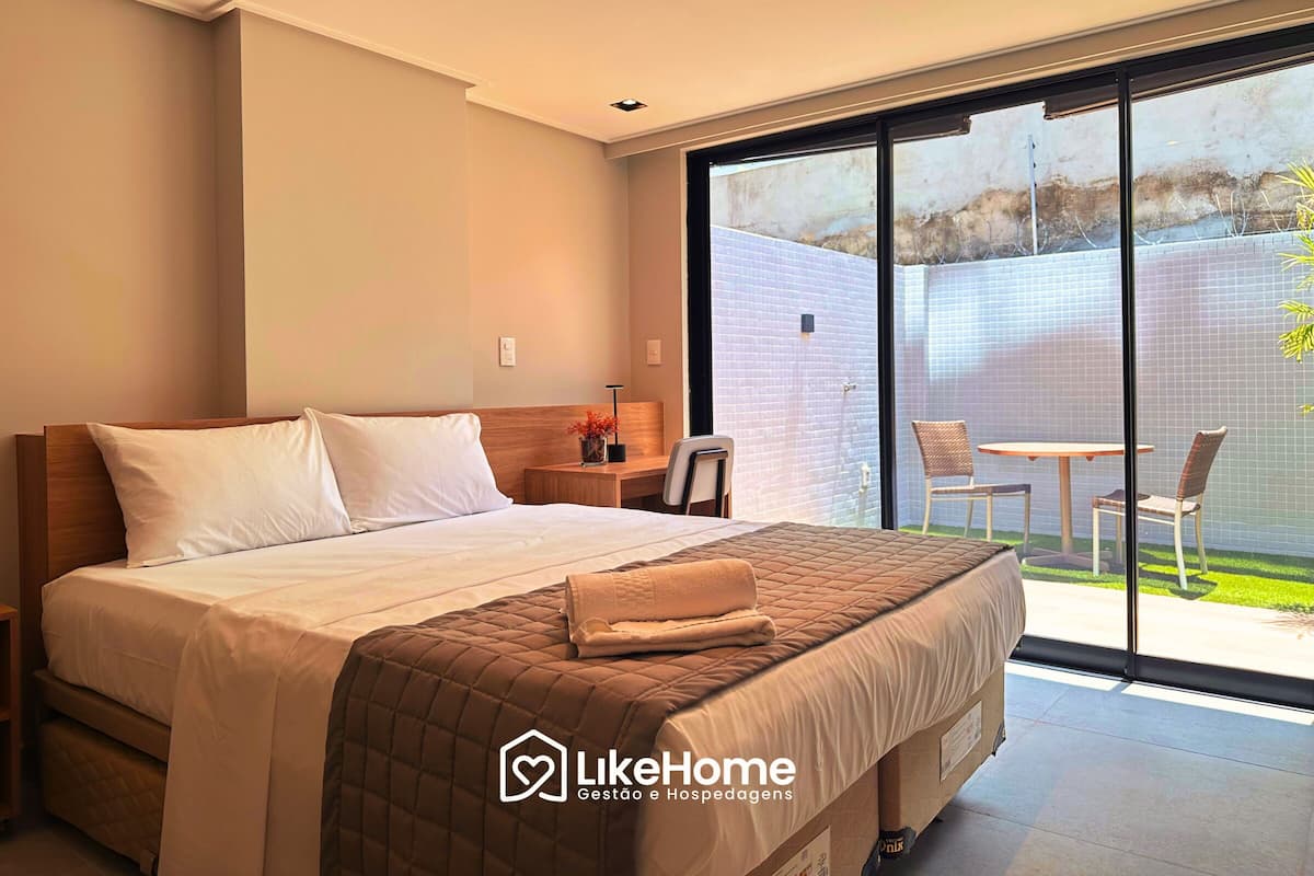 Une chambre d’hôtel avec un grand lit, un petit bureau et une vue sur un jardin, accessible par une porte-fenêtre coulissante.