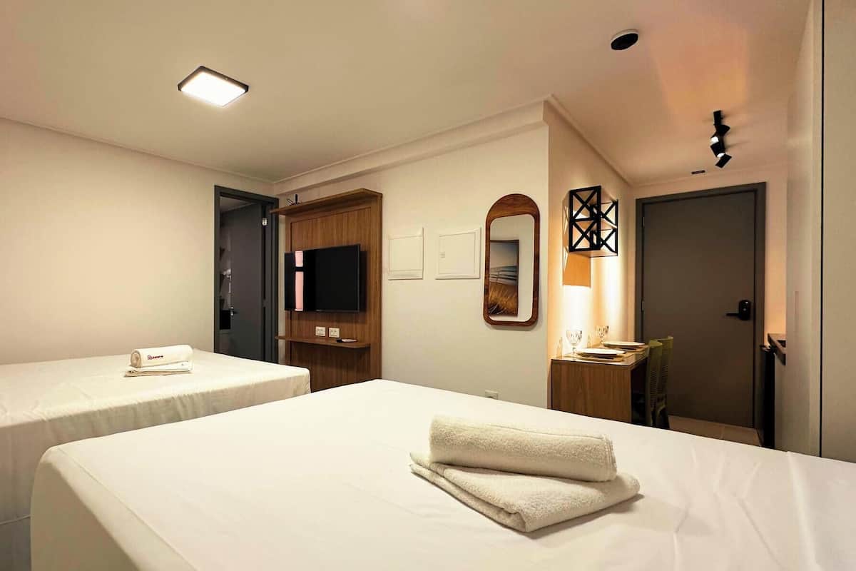 Une chambre d’hôtel avec deux lits, une télévision, un miroir et une porte.