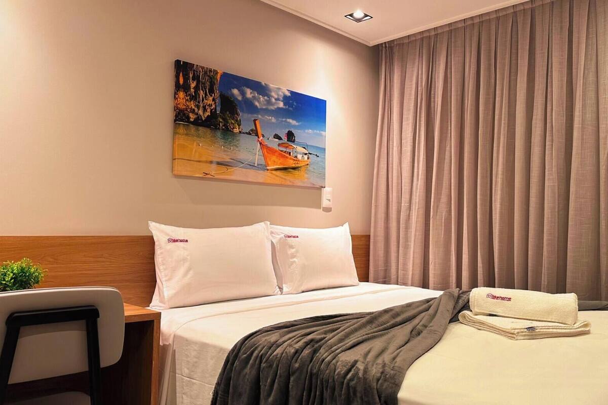 Une chambre d’hôtel avec un lit, un tableau représentant une scène de plage, un bureau et une chaise.