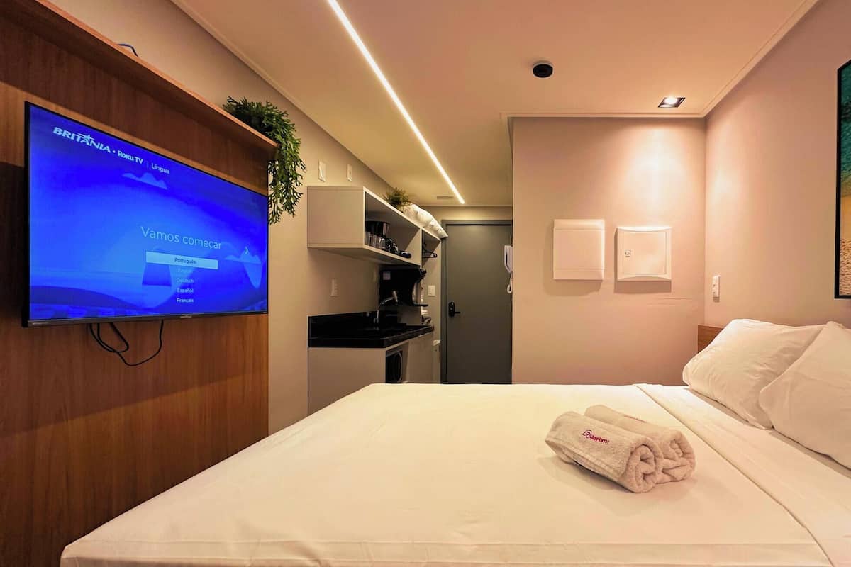 Une chambre d’hôtel avec un lit, un téléviseur affichant un écran de sélection de langues, une petite kitchenette et un tableau au mur.