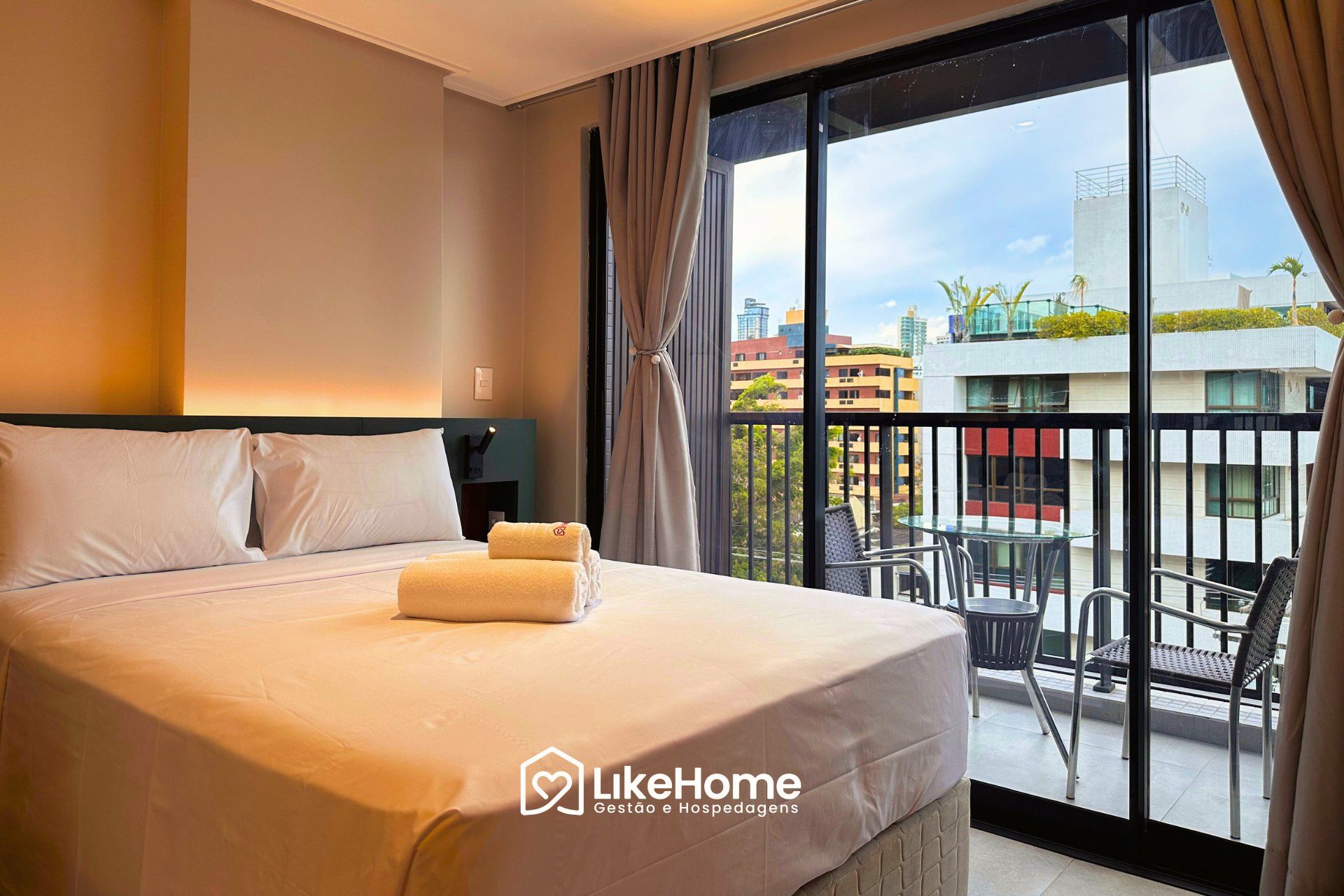 Ein Hotelzimmer mit Bett, einem Balkon mit Tisch und Stühlen sowie Blick auf die Stadtlandschaft.