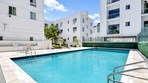 Piscina retangular com água azul cristalina, rodeada por um deck revestido com azulejos.