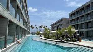 A swimming pool adjacent to modern buildings with balconies, surrounded by palm trees and outdoor seating. - Porto 2 Life Resorts (Ipojuca)
