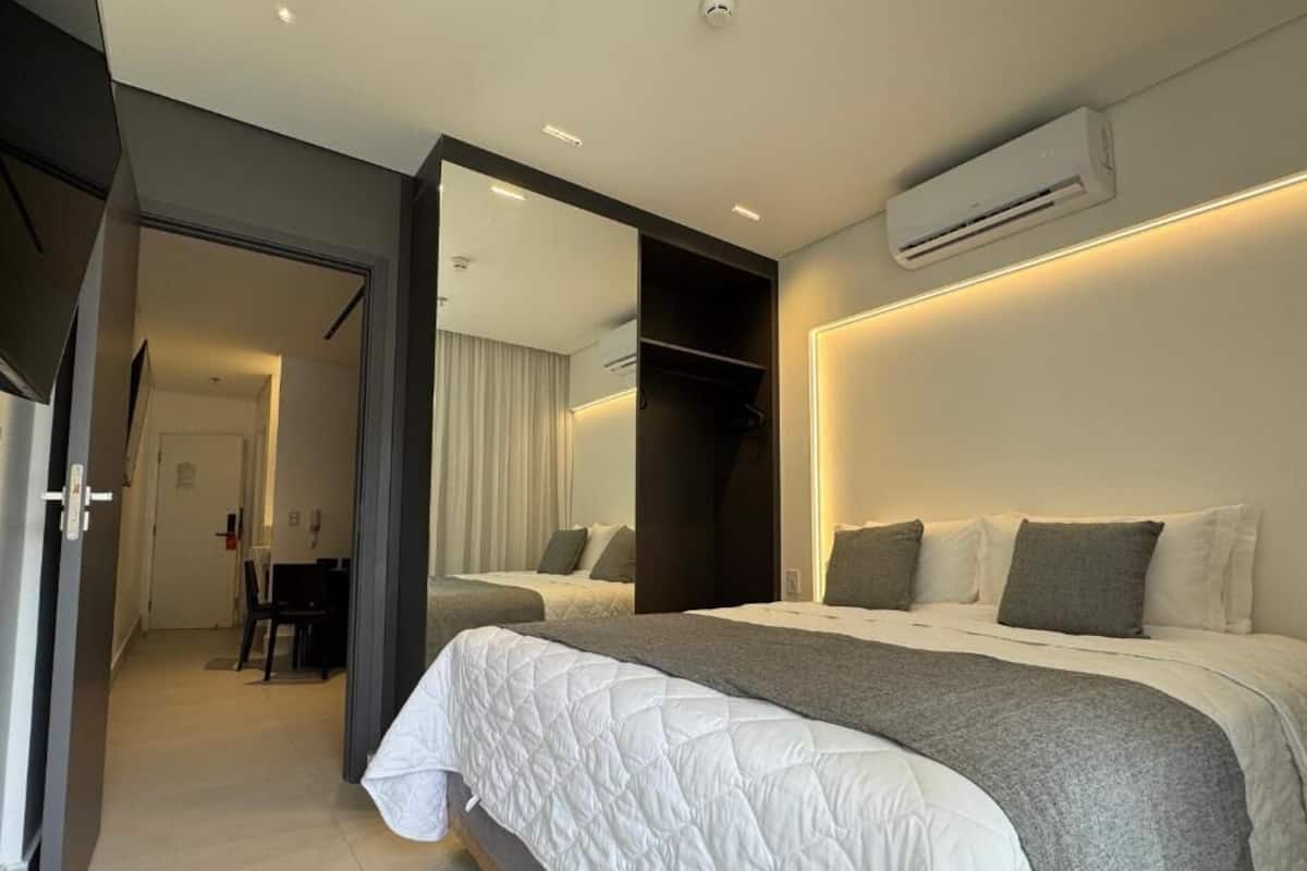 A modern bedroom with a large bed, a bedside table, a mirror, and an air conditioning unit.