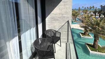 Un balcon avec deux chaises noires, un mur en béton et une vue sur un espace piscine agrémenté de palmiers et d’un bâtiment en arrière-plan.